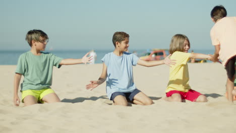 Boy-running-and-giving-five-to-friends-sitting-on-sandy-beach